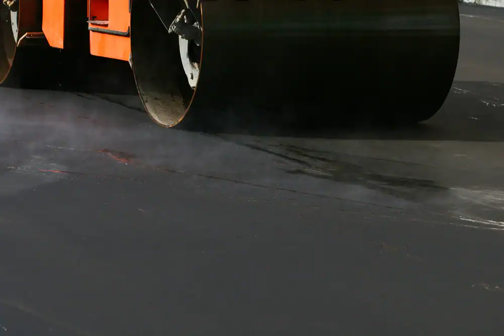 Close-up of a steamroller smoothing and compacting hot asphalt on a road in Sussex & Somerset County, NJ, with steam rising from the freshly laid surface&mdash;expertly handled by Paving Contractors Morris.