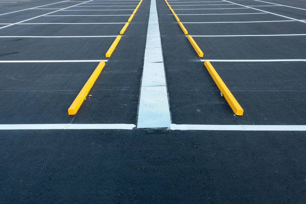 Empty parking lot with freshly painted white lines and yellow wheel stops, viewed from ground level with a concrete divider&mdash;expertly finished by top NJ paving contractors serving Sussex & Somerset County, including Morris.
